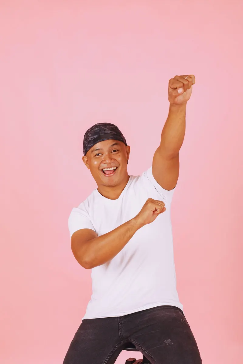 A man in a bandana cheering on a pink backdrop