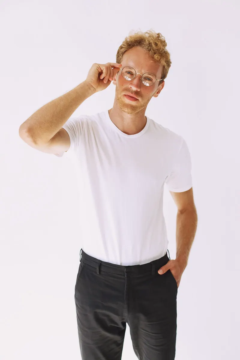 A man adjusting his glasses on a white backdrop