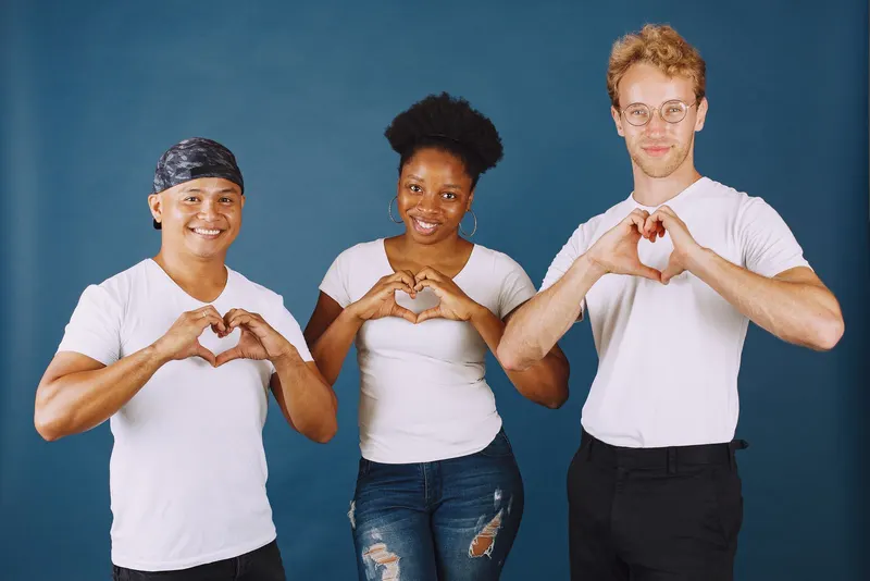 Three friends making heart shapes on a blue backdrop
